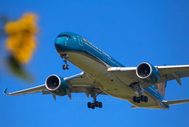 A Vietnam Airlines plane is flying with landing gear extended under a bright blue sky, HD Desktop Wallpaper