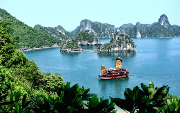 A traditional boat sails through a scenic Vietnamese bay with lush islands and clear water, 2K Desktop Wallpaper