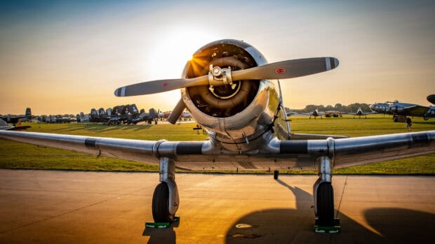 A vintage aircraft is parked on an airfield with the sun setting in the background, 2K Desktop Wallpaper