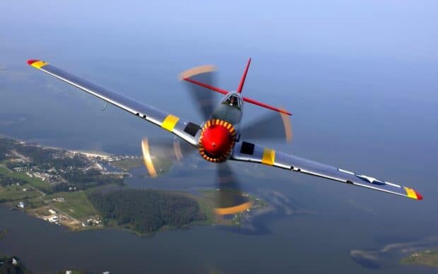 A vintage aircraft is flying low above the coastal water with a clear sky background, 2K Desktop Wallpaper