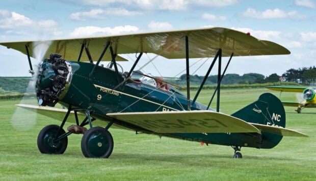 A vintage biplane aircraft is parked on a grassy airfield with a pilot inside the cockpit, HD Desktop Wallpaper PC Wallpaper