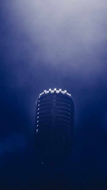 A vintage microphone stands against a blue smoky background for recording or performance, 2K Phone Wallpaper