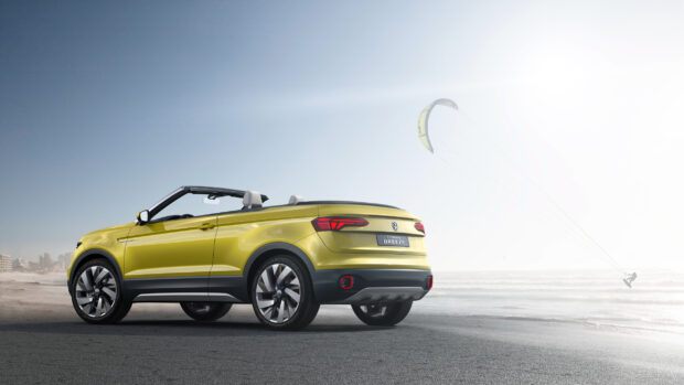 A yellow Volkswagen T Cross convertible is parked on a beach with a kite surfer in the background, 2K Desktop Wallpaper
