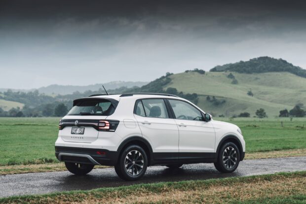 A white Volkswagen T Cross is parked on a wet road with green hills in the background, 2K Desktop Wallpaper