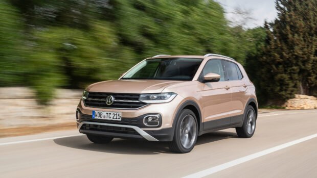A beige Volkswagen T Cross drives fast on a road with greenery in the background, 4K Desktop Wallpaper