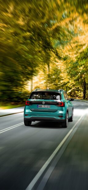 A Volkswagen T Cross is driving along a winding road surrounded by autumn trees, 2K Phone Wallpaper