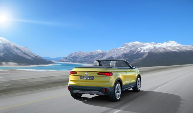 A yellow Volkswagen T Cross is driving along a scenic mountain road under a clear blue sky, HD Desktop Wallpaper