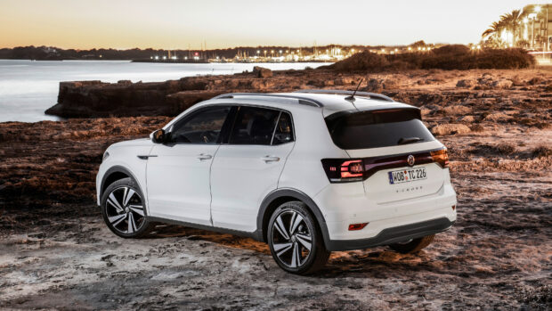 A white Volkswagen T Cross is parked on a rocky shore with a sunset over the water in the background, 4K Desktop Wallpaper