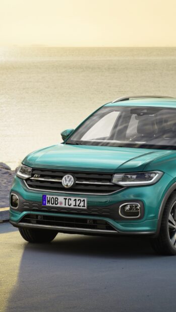 A teal Volkswagen T Cross is parked near the shoreline with the ocean in the background, 2K Phone Wallpaper