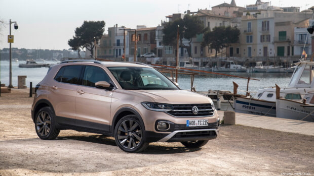 A beige Volkswagen T Cross is parked near boats by the water in a coastal town, 4K Desktop Wallpaper