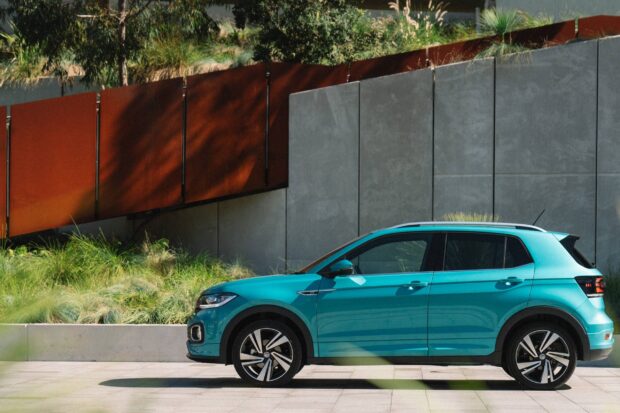 A teal Volkswagen T Cross is parked next to a modern concrete and rust colored wall, 2K Desktop Wallpaper