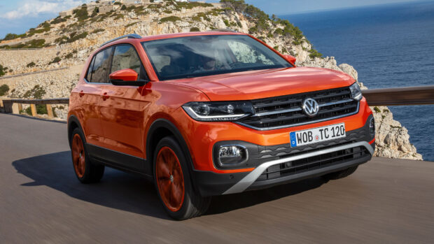A bright orange Volkswagen T Cross drives along a rocky coastline under a clear sky, HD Desktop Wallpaper