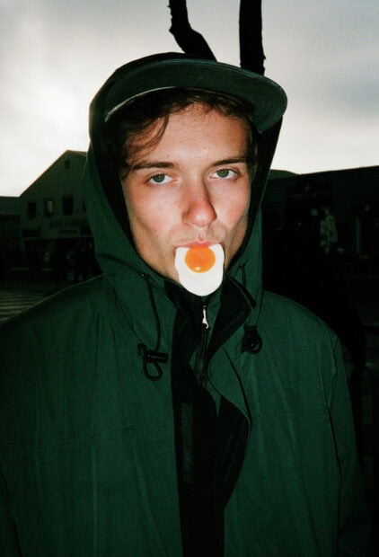 A Vundabar Band member wears a hooded jacket with an egg accessory in their mouth, HD Mobile Wallpaper