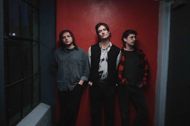 Three members of Vundabar band stand against a red wall in a moody hallway setting, 2K Desktop Wallpaper