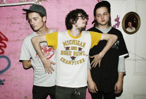 Three young men of Vundabar band standing against a pink wall with artistic elements, HD Desktop Wallpaper