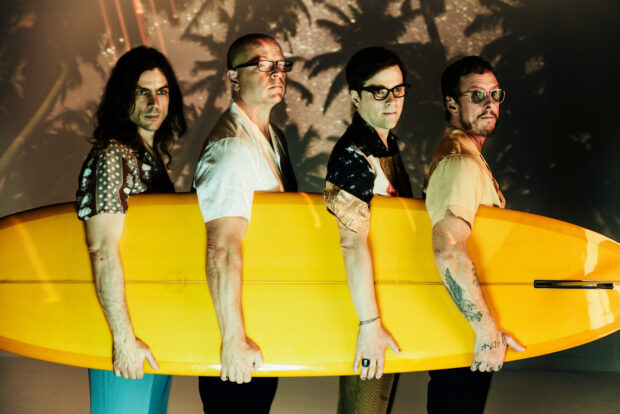 The Weezer band members stand together holding a yellow surfboard with shadows in the background, HD Desktop Wallpaper