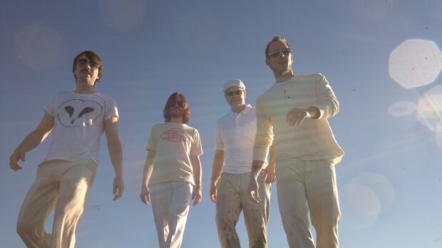 Four band members of Weezer are walking under a clear sky wearing casual outfits, HD Desktop Wallpaper