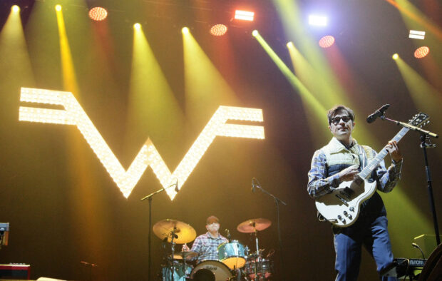 A guitarist and drummer perform on stage with the illuminated Weezer logo behind them, HD Desktop Wallpaper