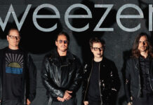 The Weezer band members standing together with a dark wall background, 2K Desktop Wallpaper