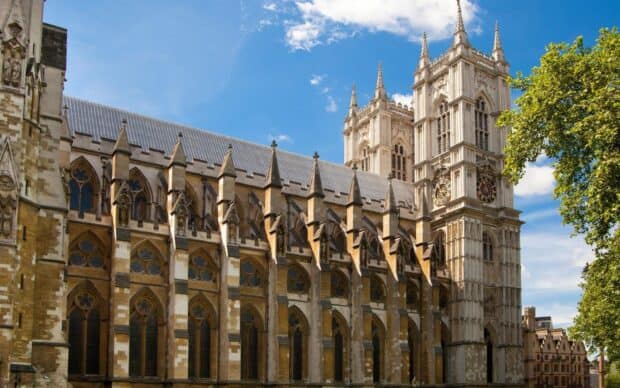 The towering facade of Westminster Abbey shines under a blue sky with greenery nearby, HD Desktop Wallpaper
