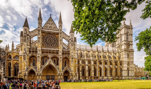 A large group of people gathers in front of Westminster Abbey showcasing its detailed gothic architecture, 2K Desktop Wallpaper