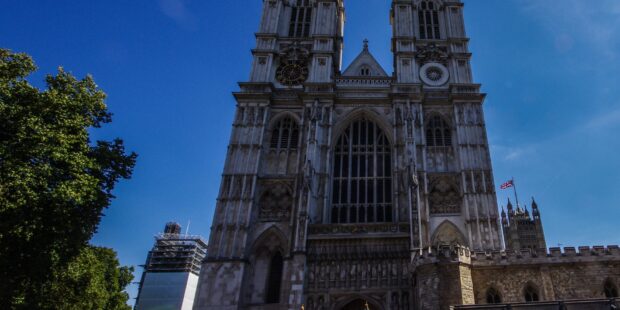 The Westminster Abbey clock tower stands tall with a clear blue sky background and trees nearby, 2K Desktop Wallpaper