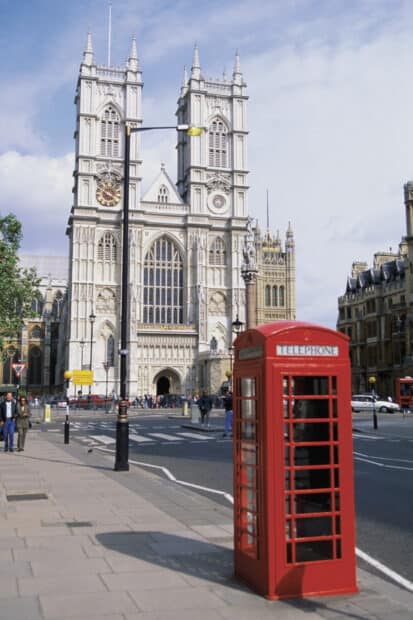 A red phone booth stands near Westminster Abbey under a clear sky in London, HD Mobile Wallpaper