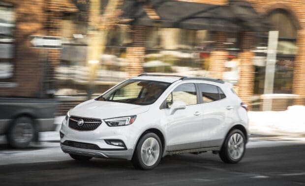 A white Buick Encore drives past brick buildings on a busy urban street scene, HD Desktop Wallpaper