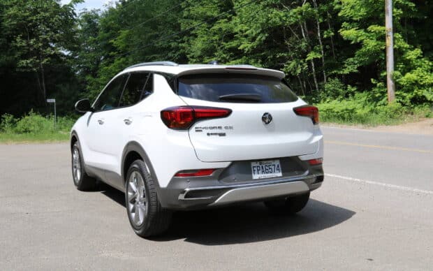 A white Buick Encore is shown from the rear while parked on a paved road surrounded by trees, HD Desktop Wallpaper