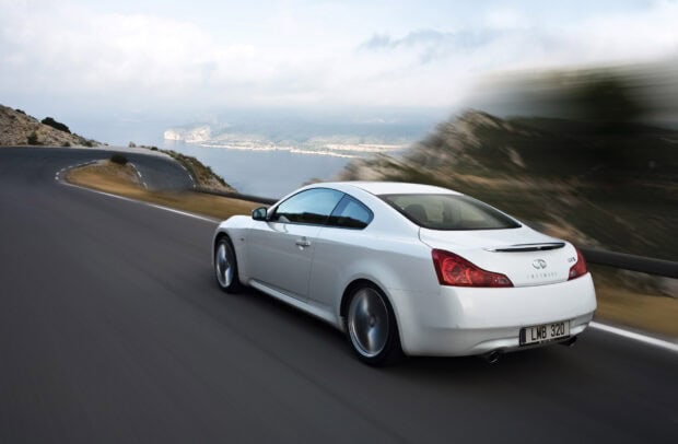 A white Infiniti G37 car is driving fast along a curved mountain road with scenic views, HD Desktop Wallpaper