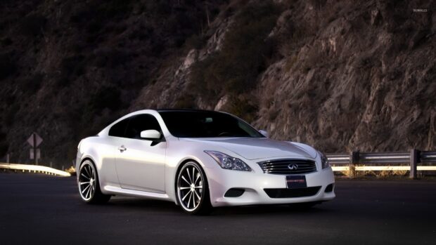 A sleek Infiniti G37 stands on a road beside rocky hills under evening light, HD Desktop Wallpaper