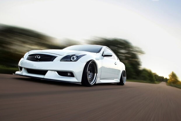 A white Infiniti G37 is driving fast on a paved road with blurred background trees, HD Desktop Wallpaper