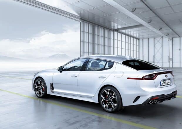 A white Kia Stinger is parked inside a spacious garage with large windows and a distant mountain view, HD Desktop Wallpaper