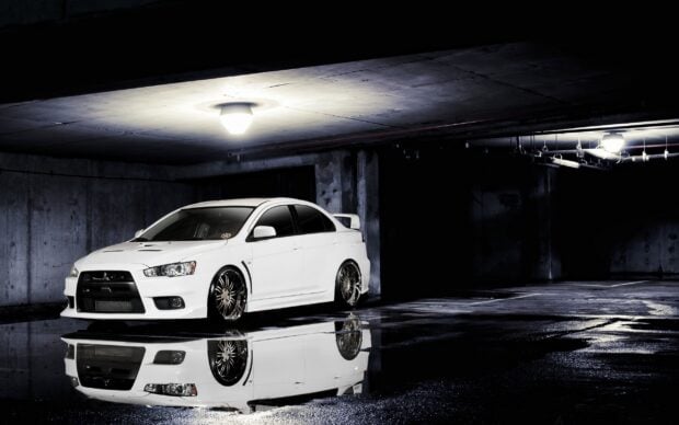 A white Lancer Evo car is parked inside a dimly lit garage with its reflection visible on the wet floor, 2K Desktop Wallpaper