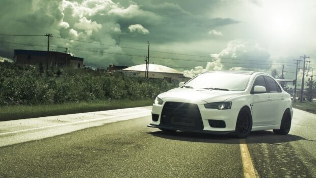 A white Lancer Evo is parked on the road under a cloudy sky with green bushes in the background, HD Desktop Wallpaper