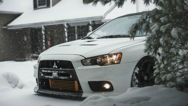 A white Lancer Evo covered in snow is parked near a house during snowfall, HD Desktop Wallpaper