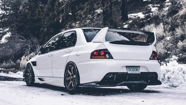 A white Lancer Evo is parked on a snow covered road surrounded by trees and hill slopes, 2K Desktop Wallpaper