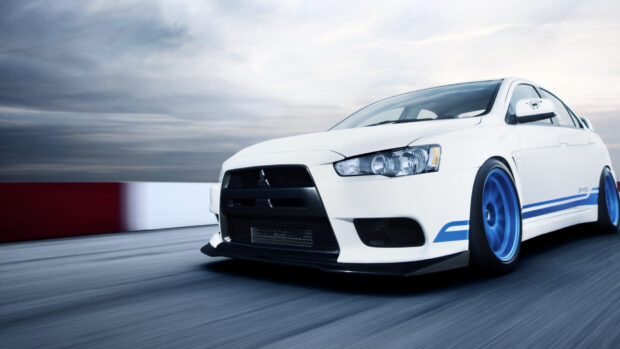 A white Lancer Evo is speeding on a race track with blue rims and a cloudy sky, HD Desktop Wallpaper