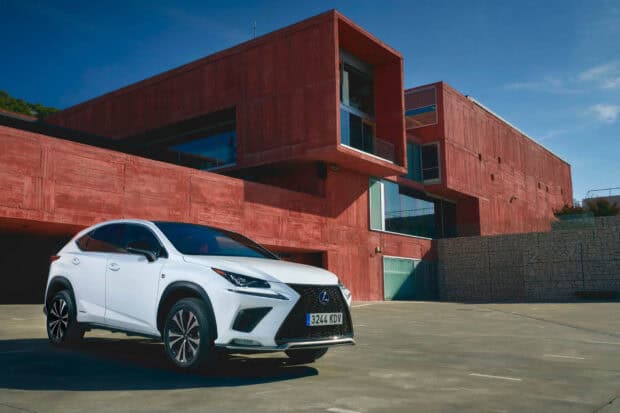 A white Lexus NX stands near a large rustic red building under a clear blue sky, 2K Desktop Wallpaper