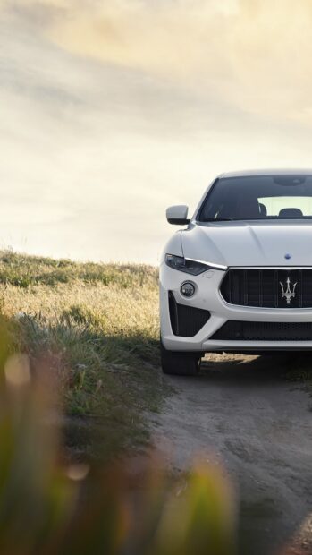 A white Maserati Levante is parked on a dirt path surrounded by grass under a cloudy sky, 2K Mobile Wallpaper