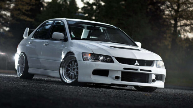 A white Mitsubishi Lancer Evo is parked on a dark gravel road with trees in the background, HD Desktop Wallpaper