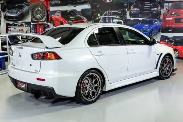 A white Mitsubishi Lancer Evo is parked indoors with car posters on the walls, HD Desktop Wallpaper