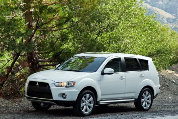 A white Mitsubishi Outlander is parked on a road surrounded by green trees and nature, 2K Desktop Wallpaper
