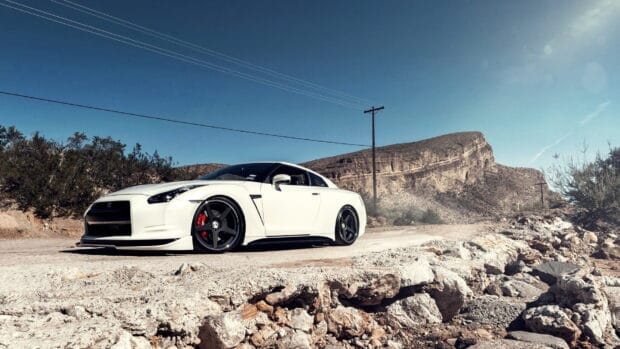 A white Nissan GT R is parked on a rocky desert road under a clear blue sky, HD Desktop Wallpaper