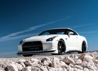 White Nissan GT R sports car is parked on rocky ground under a clear blue sky, 2K Desktop Wallpaper
