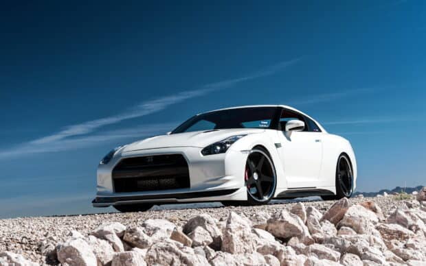 White Nissan GT R sports car is parked on rocky ground under a clear blue sky, 2K Desktop Wallpaper