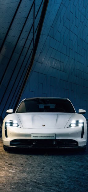 A white Porsche Taycan is parked on a stone ground with a blue geometric wall in the background, HD Mobile Wallpaper