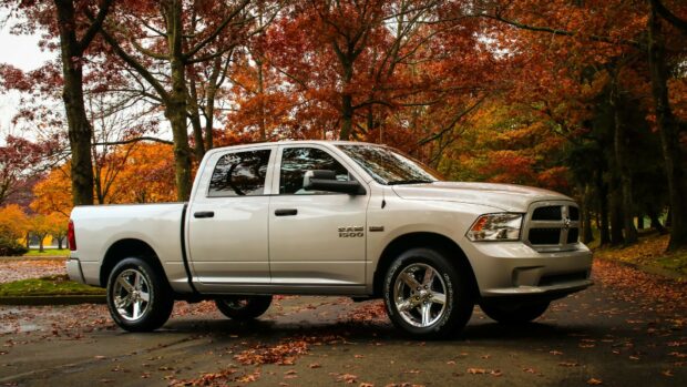 A white Ram pickup truck is parked on a road covered with fallen leaves under orange autumn trees, HD Desktop Wallpaper