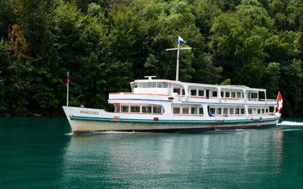A white ferry sails smoothly on calm turquoise water surrounded by lush green trees in the background, 2K Desktop Wallpaper