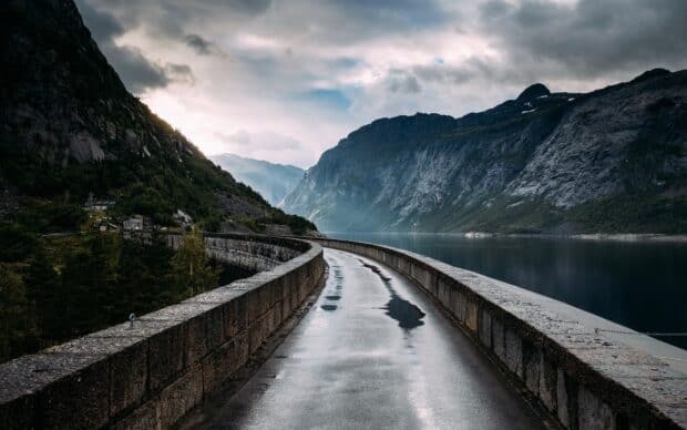 A winding road runs beside the calm Norwegian fjords under a cloudy sky, 2K Desktop Wallpaper